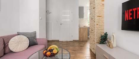 Una sala moderna con un sofá, una mesa de centro de vidrio con fruta, una pared de acento de piedra y un televisor mostrando 'NETFLIX'.