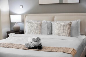 A neatly made bed with rolled towels and a black hairbrush, a bedside lamp, and patterned pillows on a headboard. - StayShort - Modern and Chic Studio in Downtown with Burj Khalifa Views! (Downtown)