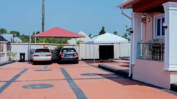 A parking area with two cars, a covered outdoor seating area, and a building with a white facade.