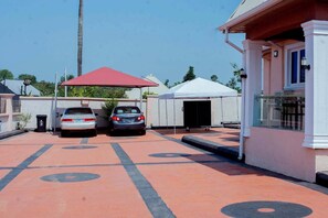 Un estacionamiento con dos autos, un espacio de estar al aire libre techado y un edificio de fachada blanca.