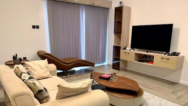 A modern living room with a sofa, a coffee table, a TV, and a sliding door. - FEYINTOLA SHORTLET APARTMENT (Ondo)