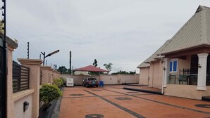 A gated parking area with a car parked in the center, surrounded by buildings with a beige facade and a red roof. - FEYINTOLA SHORTLET APARTMENT (Ondo)