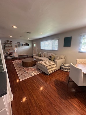 A modern living room with a sofa, ottoman, coffee table, and a dining area with a table and chairs. - Backyard Oasis with Fire Pit, Grill & Outdoor TV, 15 Min to La Jolla (San Diego)