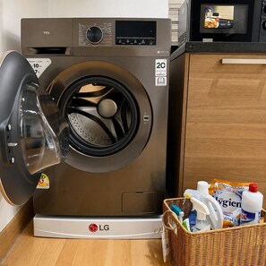 A front-loading LG washing machine with a basket of laundry detergent and cleaning supplies beside it. - One quiet bedroom apartment with amazing balcony views next to Nana and Soi 11 (Khet Khlong Toei)