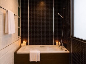 Et moderne badeværelse med badekar, to vægmonterede lys og en brusehoved.