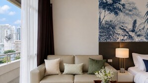 Ein Hotelzimmer mit Sofa, Nachttisch mit Lampe, Bett und Blick auf die Stadt.