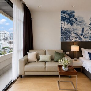 Ein Hotelzimmer mit Sofa, Nachttisch mit Lampe, Bett und Blick auf die Stadt.