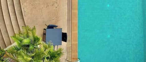 An aerial view of a swimming pool with lounge chairs and palm trees.