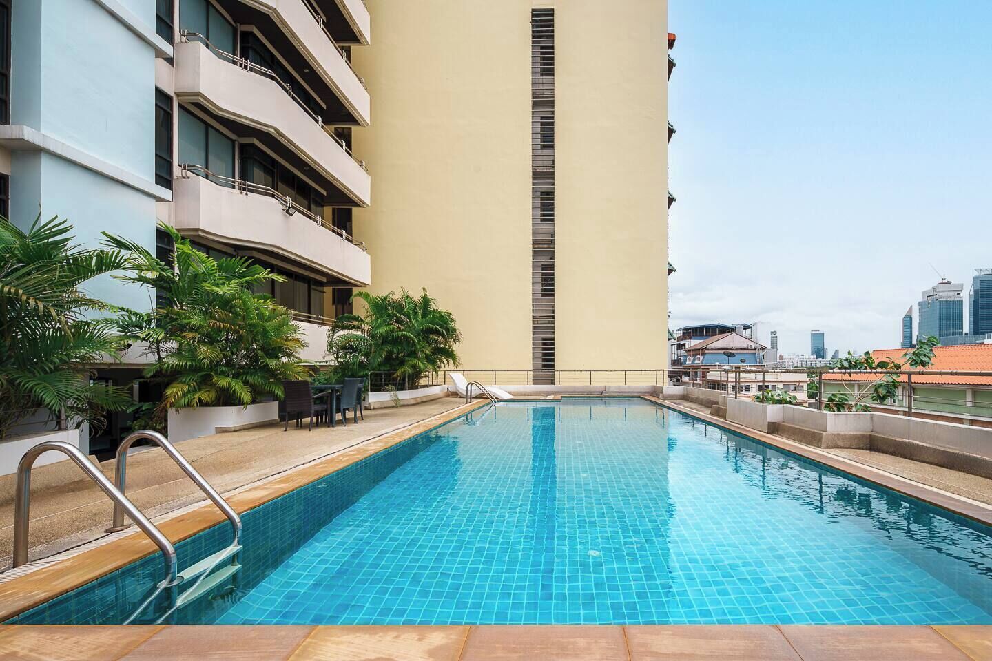 Piscina en la azotea con vista a un edificio alto, asientos exteriores y plantas en macetas.