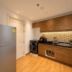 Eine moderne Küche mit Holzschränken, einem Edelstahlkühlschrank, einer Waschmaschine und einer gefliesten Rückwand.
