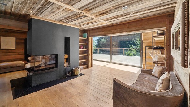 A modern interior with a wooden ceiling, a fireplace, a sofa, and a large window offering a view of greenery. - The Crest by Mrs Miggins ****Welcome to The Crest by Mrs Miggins ****, an exceptional chalet nestled (Crans-Montana)