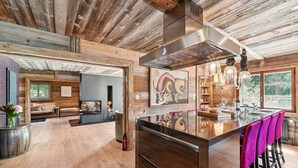 A spacious living area with a wooden ceiling, a fireplace, and a bar area with stools. - The Crest by Mrs Miggins ****Welcome to The Crest by Mrs Miggins ****, an exceptional chalet nestled (Crans-Montana)