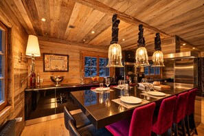 Ein Holzblockhaus-Interieur mit einer zentralen Kochinsel, Barhocker und einem Esstisch für vier Personen.