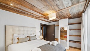 A bedroom with a large bed, wooden ceiling beams, a door, and a shelf unit. - The Crest by Mrs Miggins ****Welcome to The Crest by Mrs Miggins ****, an exceptional chalet nestled (Crans-Montana)