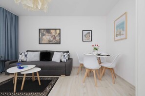 A modern living room with a grey sofa, a dining table with white chairs, and two framed pictures on the wall. - Family Apartment with a Balcony Near the Underground Ursynow (Warszawa)