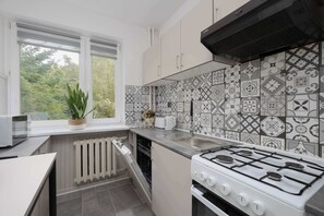A modern kitchen with a gas stove, white cabinets, and patterned backsplash tiles. - Family Apartment with a Balcony Near the Underground Ursynow (Warszawa)