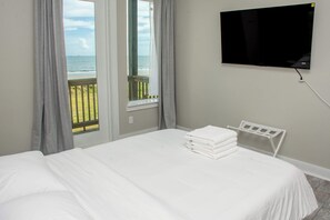 Un dormitorio con cama, televisor montado en la pared y vista al mar a través de una ventana.