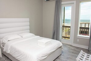 A hotel room with a large bed, a view of the ocean, and a balcony with a wooden railing.
