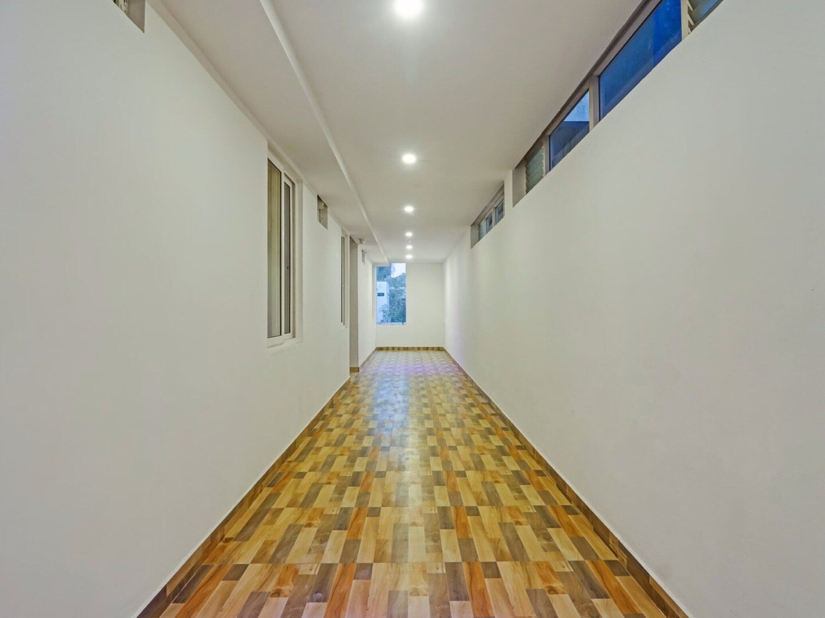 A corridor with a patterned wooden floor, white walls, and a window on the right.