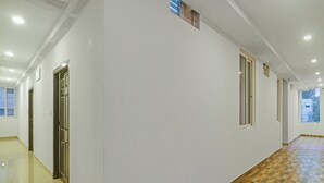 Un couloir aux murs blancs, avec un sol à carreaux et des portes sur le côté gauche.