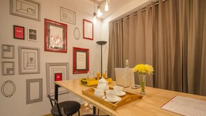 Eine moderne Küche mit Holztischplatte, zwei schwarzen Stühlen, einer Ablage mit weißen Tassen und einer Flasche sowie gerahmten Bildern an der Wand.