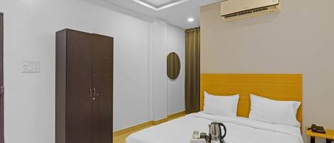 A hotel room with a bed, a wardrobe, an air conditioning unit, and a bedside table with a phone.