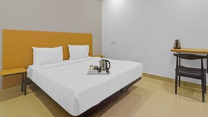 A hotel room with a bed, a bedside table, a chair, a ceiling fan, and a small table with a kettle and cups.