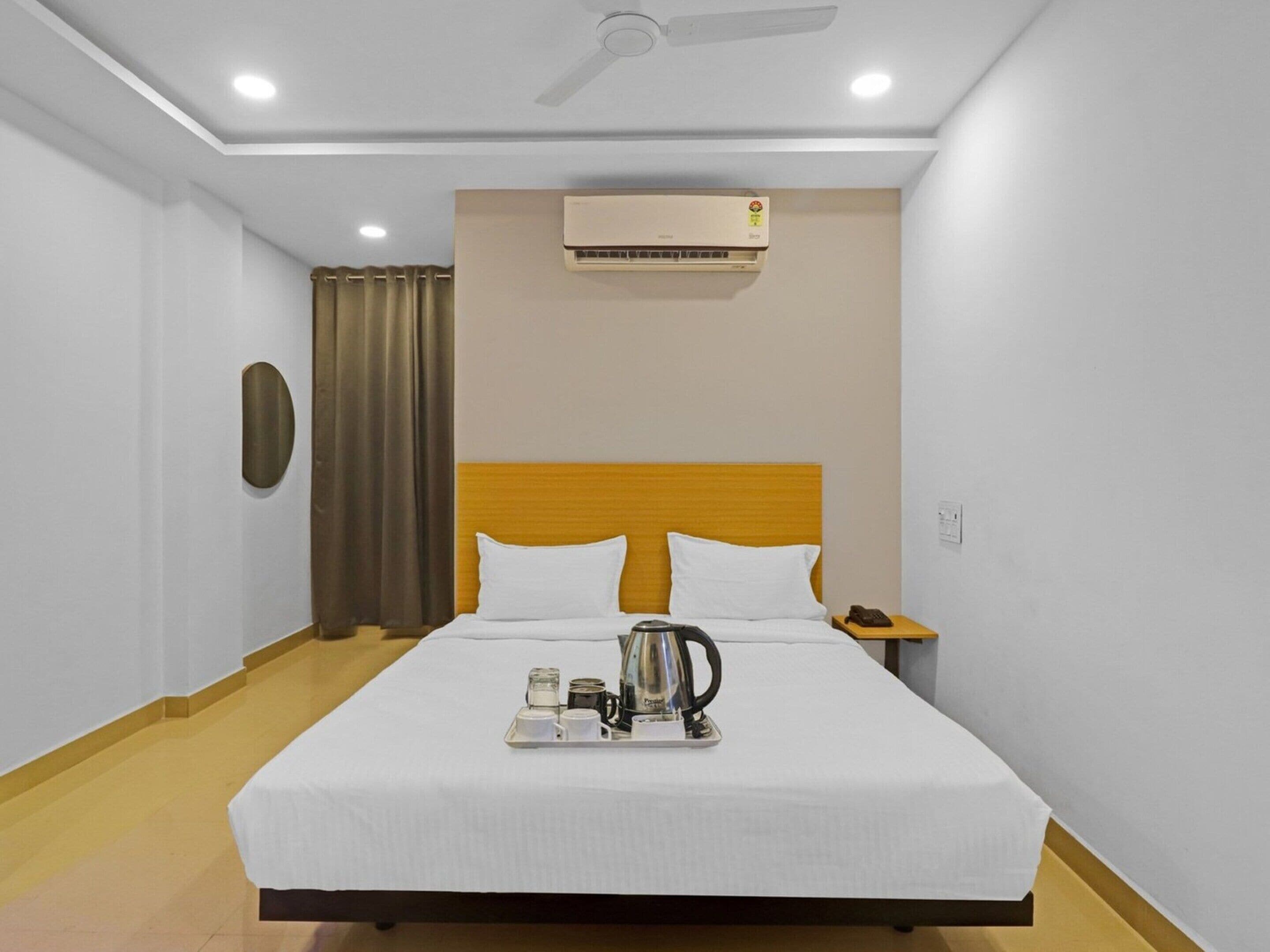 A hotel room with a bed, a nightstand, a telephone, an air conditioning unit, and a ceiling fan.