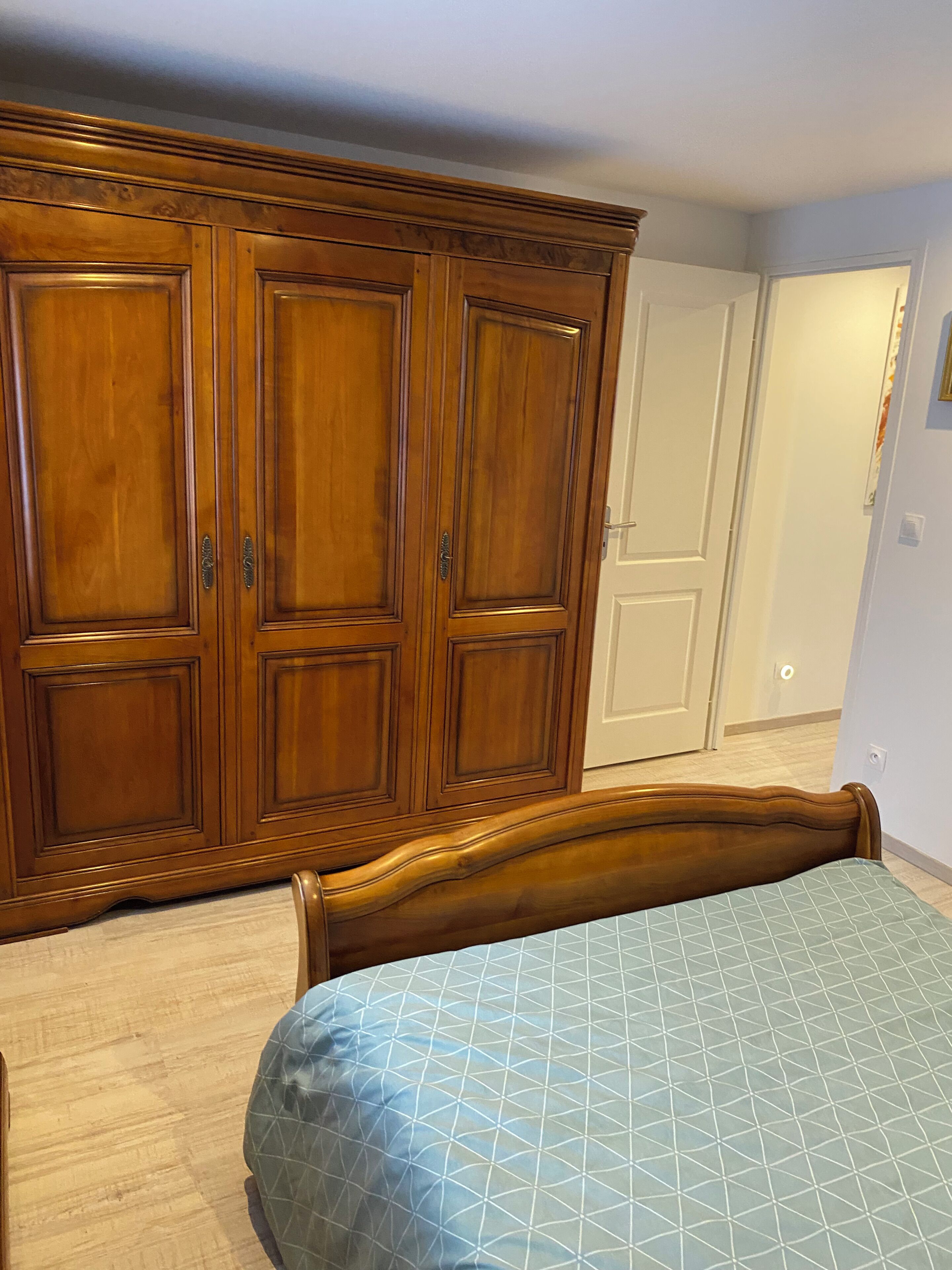A bedroom with a large wooden wardrobe, a bed with a patterned bedspread, and a white door in the background.