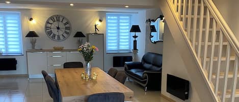 A spacious living area with a dining table, chairs, a sofa, a staircase, and a large wall clock.