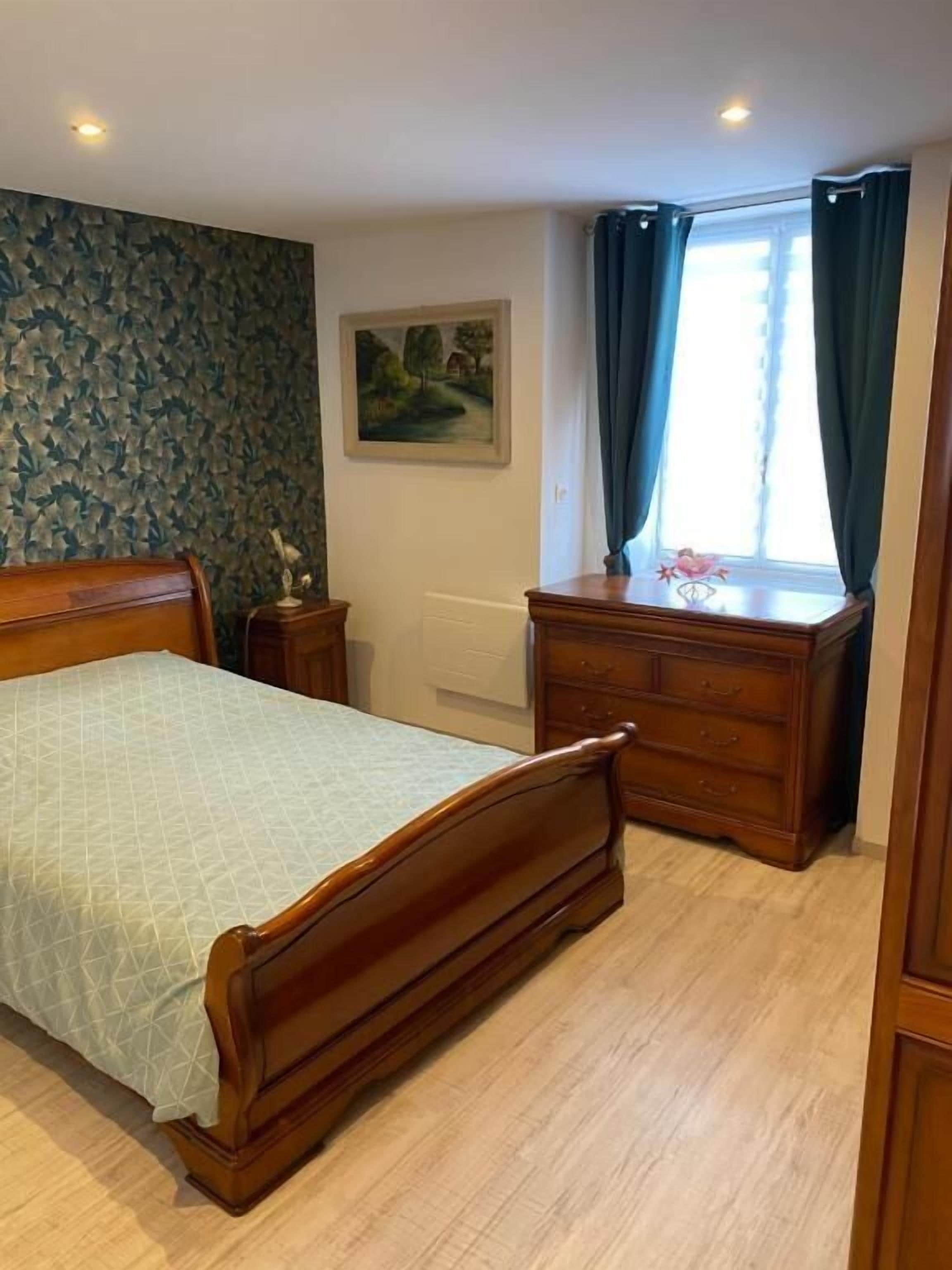 A bedroom with a wooden bed, a dresser, a radiator, and a window with curtains.
