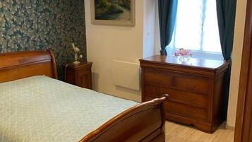 A bedroom with a wooden bed, a dresser, a radiator, and a window with curtains.