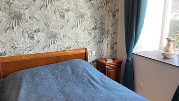 A bedroom with a bed, a nightstand, a window with curtains, and a wall with a leaf pattern.