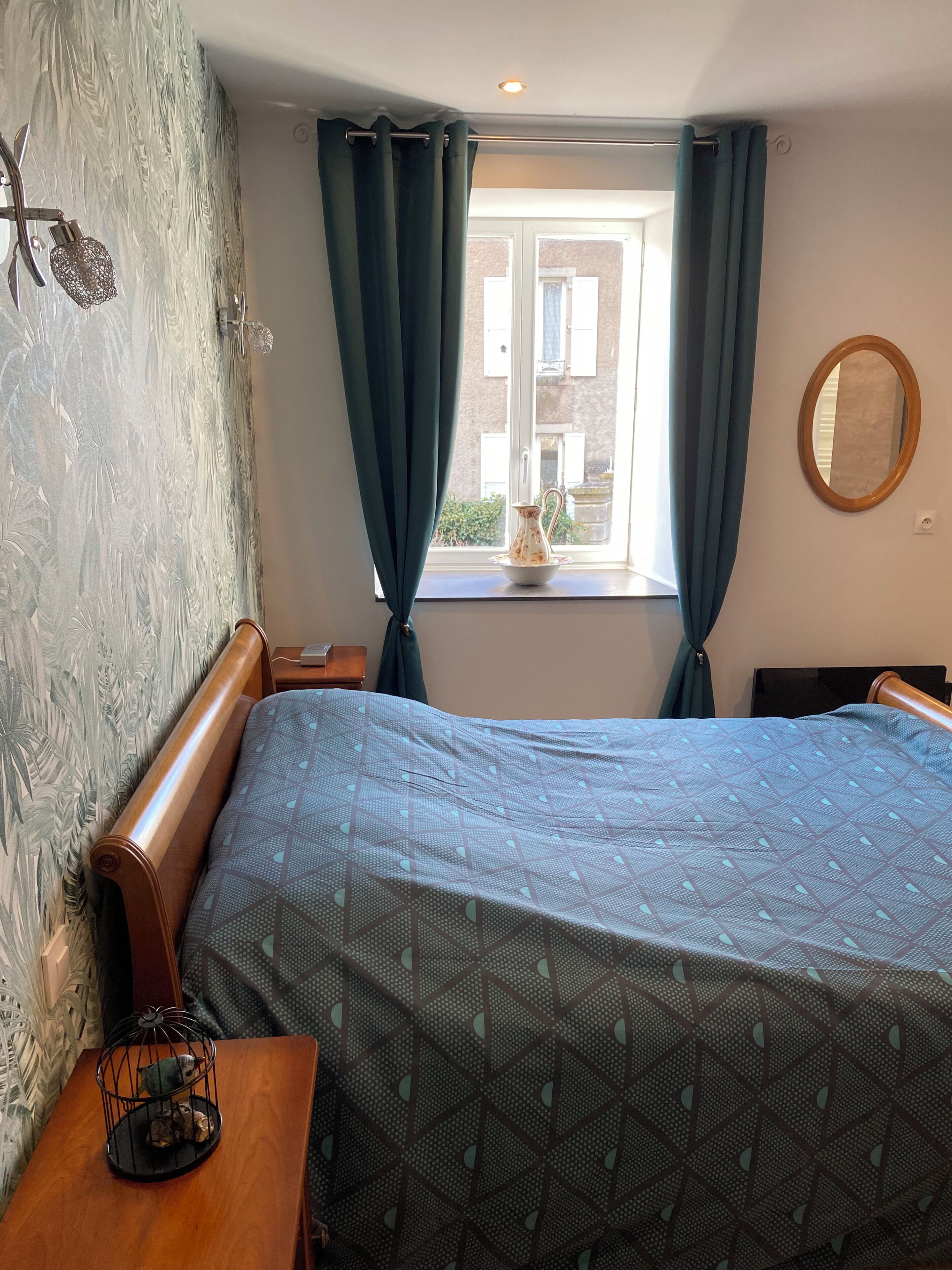 Een slaapkamer met een bed, een raam met gordijnen, een houten hoofdeinde, een nachtkastje met een lamp, en een wand met een reliëf patroon.