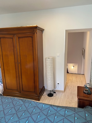A room with a wooden wardrobe, a standing lamp, a patterned rug, and a birdcage on a small table.