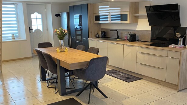 Una cocina moderna con comedor, que incluye una mesa de madera, sillas, un banco y un televisor.