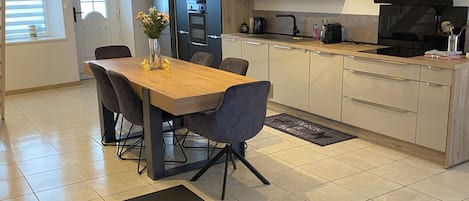 A modern kitchen with a dining area, featuring a wooden table, chairs, a bench, and a TV.