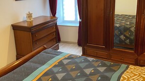 Un dormitorio con cama, cómoda, espejo y ventana con cortinas.