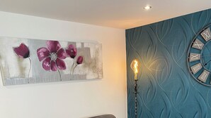 Una sala de estar con un sofá gris, una mesa de centro de vidrio, un reloj de pared y una lámpara de pie.