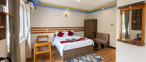 A hotel room with a wooden bed, a small table, a chair, a wardrobe, and a mirror.