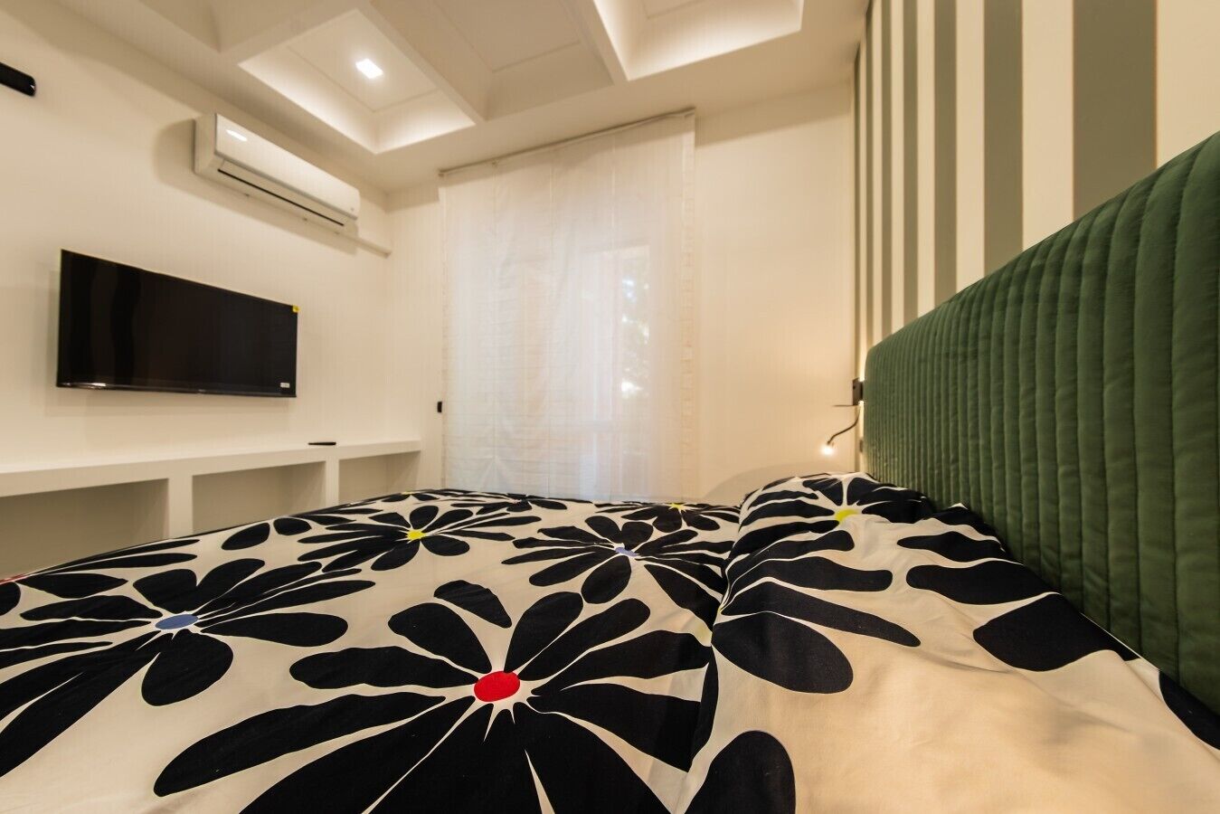 Une chambre à coucher comprenant un lit, un téléviseur à écran plat, une table de chevet et une fenêtre avec des rideaux.