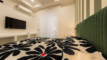 Une chambre à coucher comprenant un lit, un téléviseur à écran plat, une table de chevet et une fenêtre avec des rideaux.