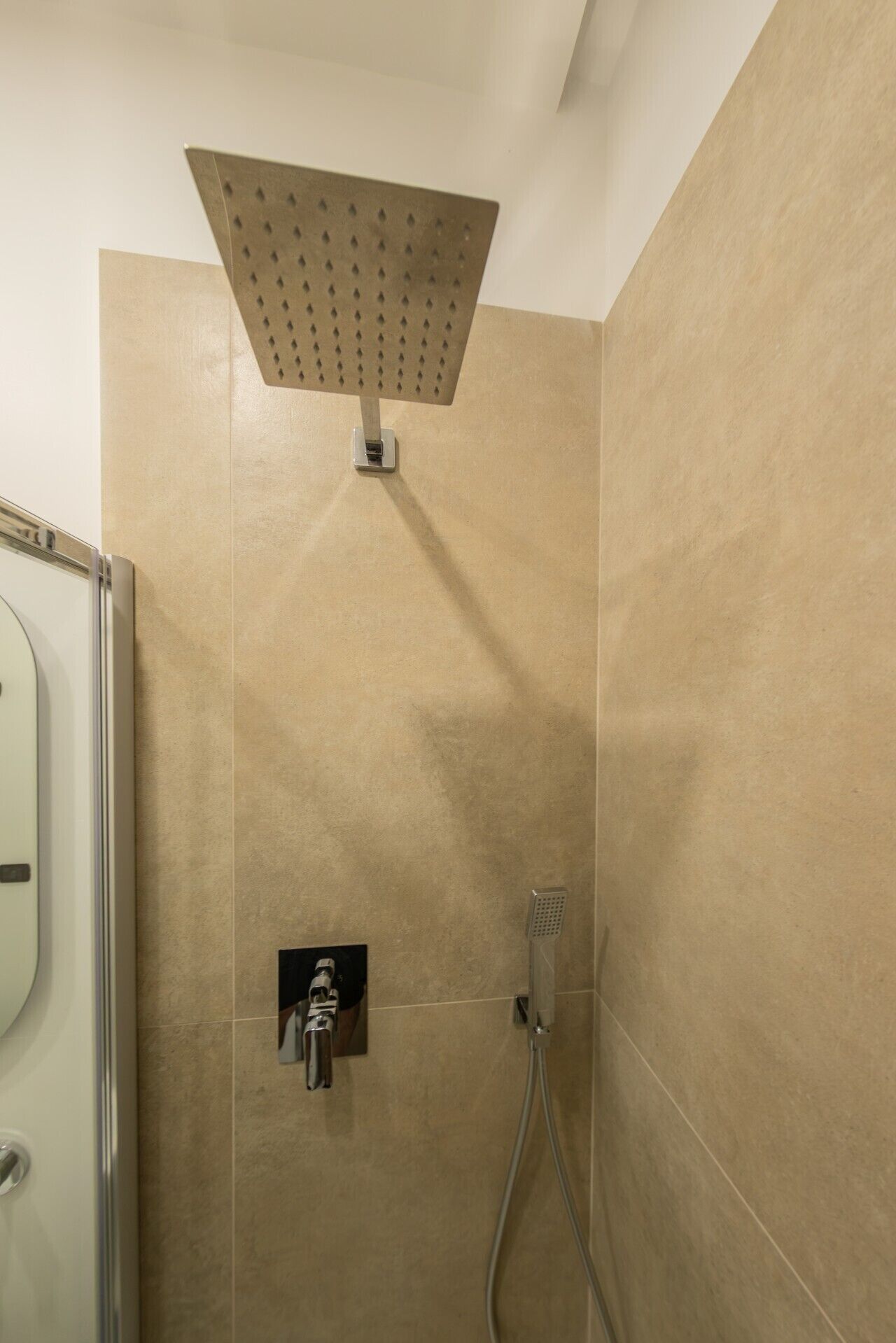 Ein Duschbereich mit einer eckigen Duschbrause, einer Handbrause und einem am Wand montierten Wasserhahn.