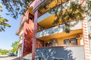 A multi-story building with balconies, a car parked in front, and trees in the background. - Apis Deluxe Double Room - Kalydon Suite (Benevento)