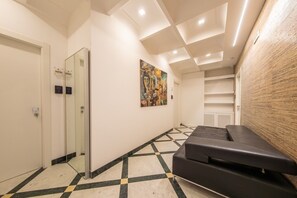 A hallway with a checkered floor, a black sofa, a painting on the wall, and an elevator. - Sofia Room - Deluxe Double Room - Kalydon Suite (Benevento)