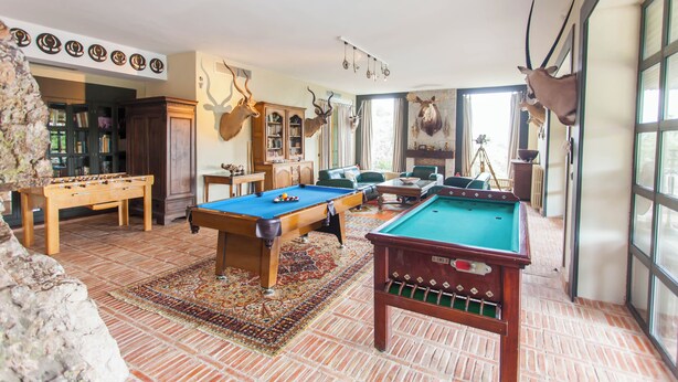 A room with two pool tables, a foosball table, and a billiards table.