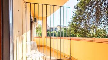 Un balcone con una sedia in vetro trasparente, un cancello in metallo e un pavimento piastrellato.