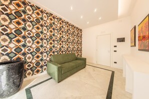 A reception area with a patterned wall, a green sofa, a reception desk, and a door. - Trajan's Arch Deluxe Junior Suite - Kalydon Suite (Benevento)