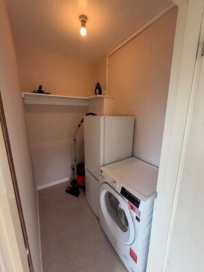 A laundry room with a washing machine and dryer, a ceiling light, and a vacuum cleaner.