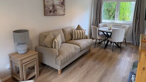 A living room with a sofa, a table with chairs, a lamp, and a painting on the wall. - The Narrows - Macaulay Letting (Rhu)